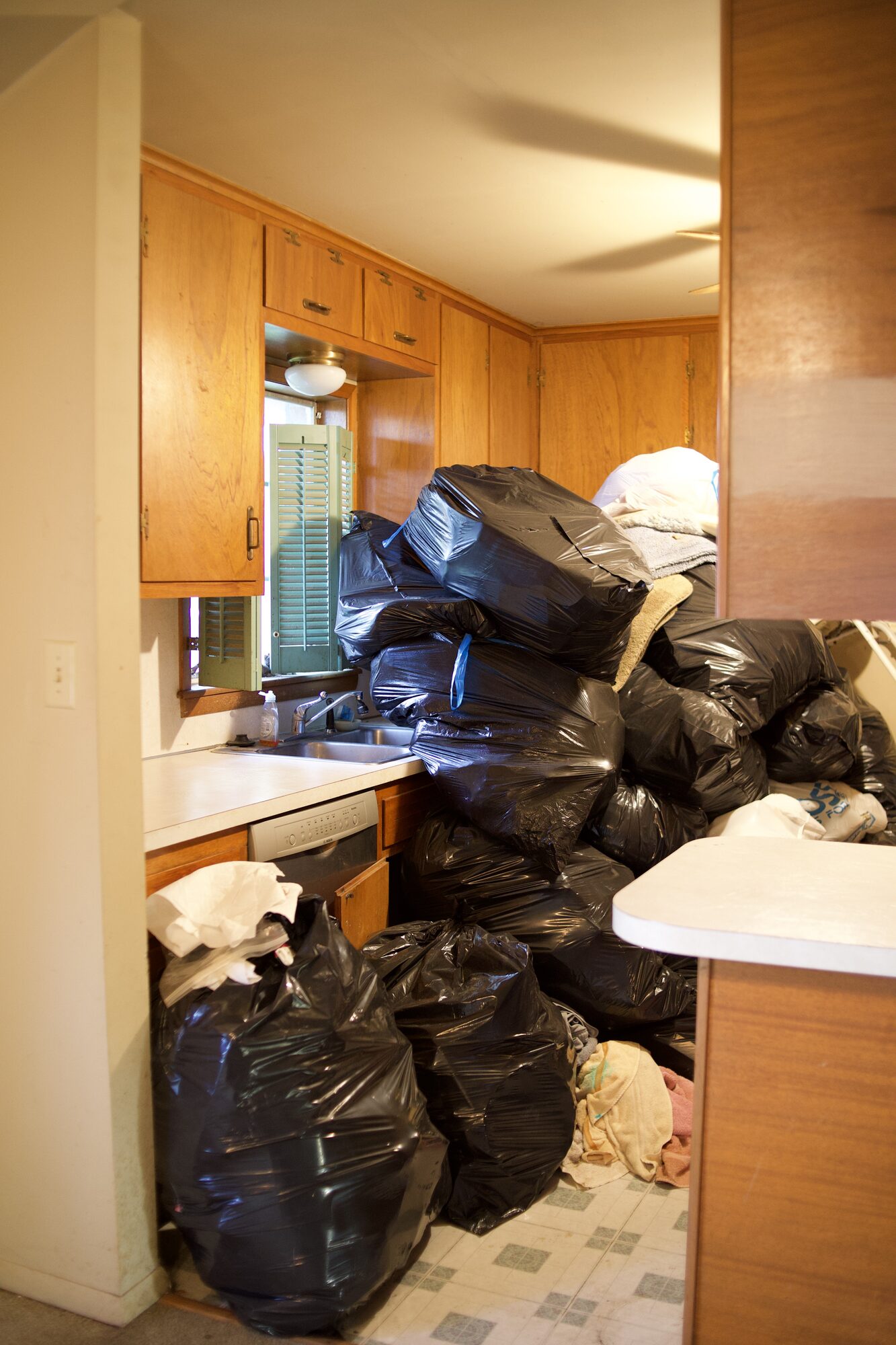 Kitchen of an inherited Tulsa house stacked with black contractor bags during an estate cleanout
